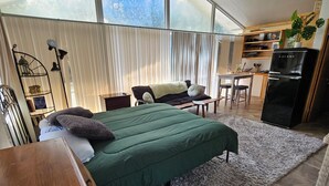 Une chambre comprenant un lit, un bureau, une chaise, un réfrigérateur et une fenêtre avec des stores.