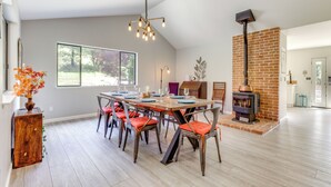 A dining area with a long table set for six, surrounded by chairs with orange cushions. A modern chandelier hangs above, and a brick fireplace is visible in the background. - Pool & Deck: Wine Country Hideaway in Middletown! (Middletown)