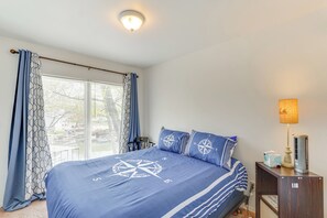 Et soveværelse med en stor seng, et natbord med lampe og et vindue med gardiner.