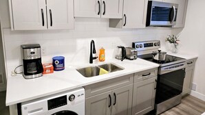 A modern kitchen with white cabinets, stainless steel appliances, a coffee maker, a toaster, and a dishwasher. - Willoughby Luxe Retreat (Langley Township)