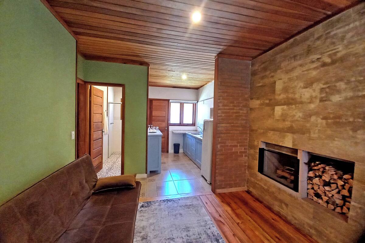 Ein gemütliches Wohnzimmer mit einer hölzernen Bank, einem Kamin und einer Küche im Hintergrund.