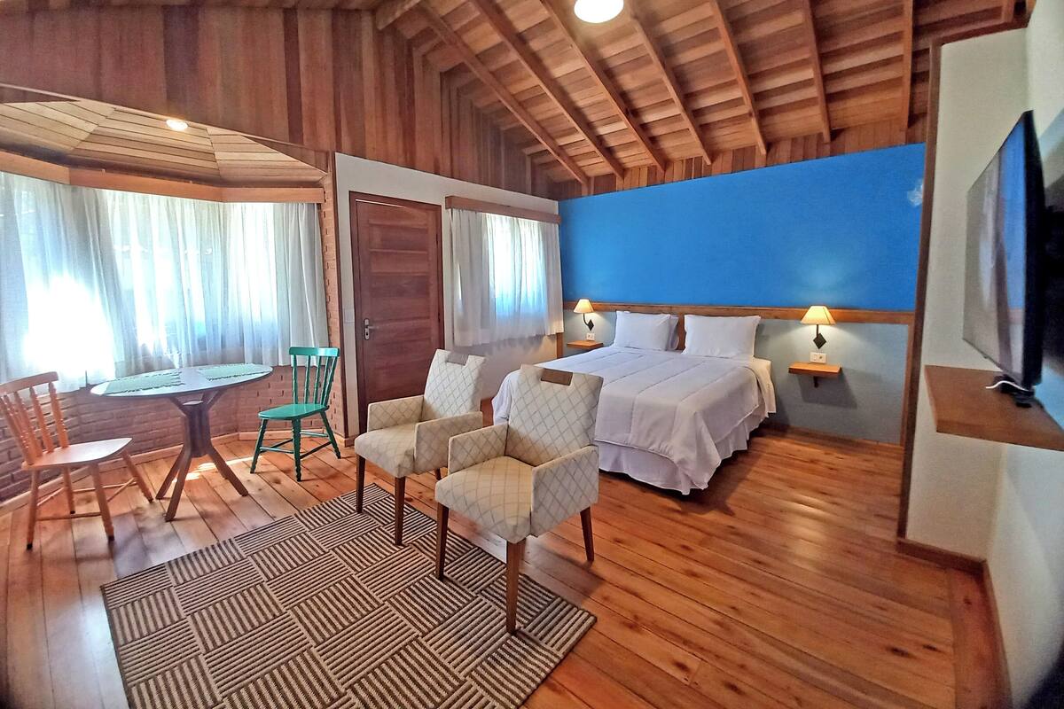 Ein Schlafzimmer mit Holzboden, einem Bett, zwei Nachttischen, einem Fernseher und einem Essbereich mit Stühlen und Tisch.