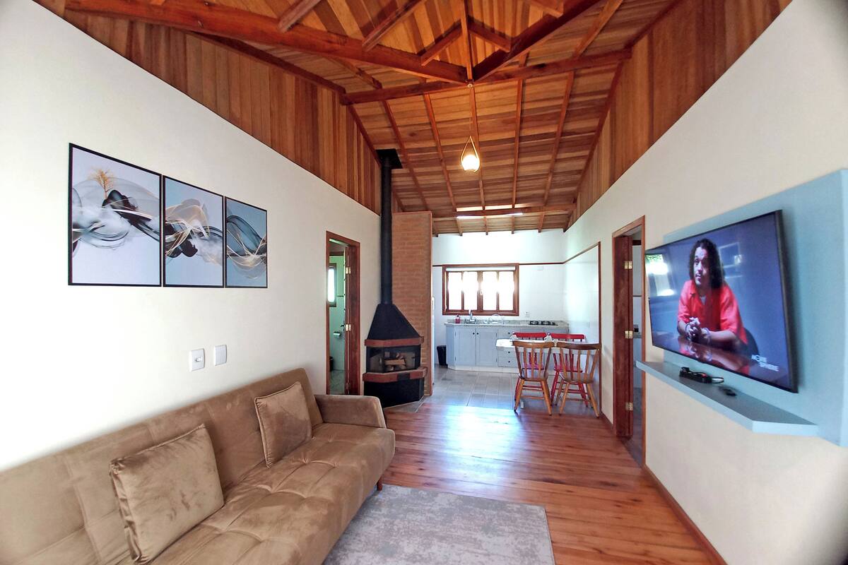 Ein geräumiges Wohnzimmer mit Holzbalkendecke, einer Couch, einem Kamin, einer Küche im Hintergrund und einem Fernseher an der Wand.