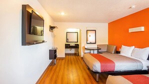 A hotel room with a bed, a desk, a chair, a mirror, and a bathroom with a sink and mirror. - Economy Hotel Kansas City (Blue Springs)