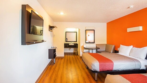A hotel room with a bed, a desk, a chair, a mirror, and a bathroom with a sink and mirror. - Economy Hotel Kansas City (Blue Springs)