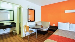 A hotel room with a bed, a small table, a chair, a sink, and a mirror. - Economy Hotel Kansas City (Blue Springs)