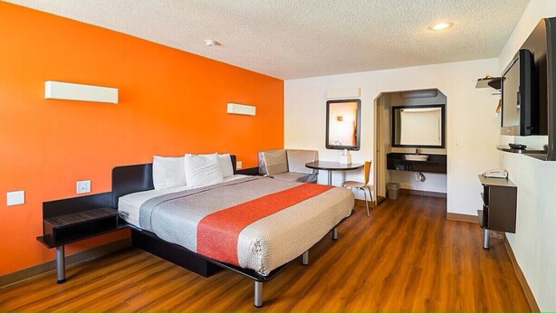 A modern hotel room with a bed, bedside tables, a desk, and a television. - Economy Hotel Kansas City (Blue Springs)