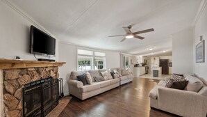 A spacious living room with a fireplace, two sofas, a television, and a ceiling fan. - Lakefront Family Retreat– Private Dock & Fire Pit​ (Kemp)