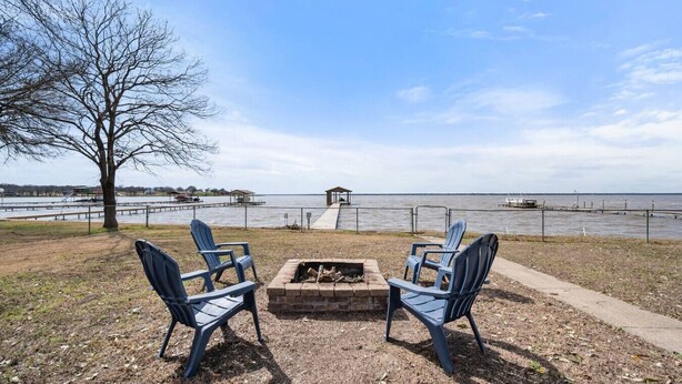 A lakeside seating area with two Adirondack chairs facing a fire pit, a dock, and a distant pier. - Lakefront Family Retreat– Private Dock & Fire Pit​ (Kemp)