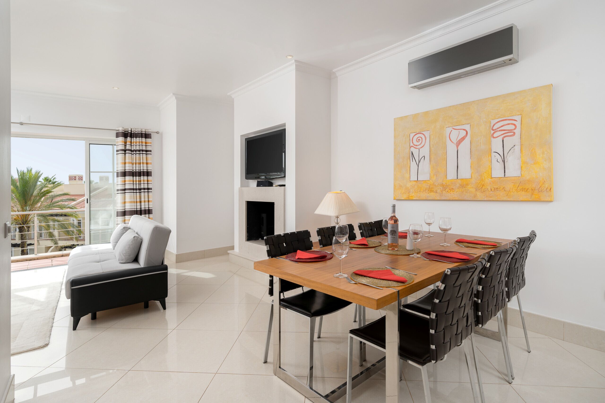 A modern dining area with a wooden table, black chairs, and a TV mounted on the wall.