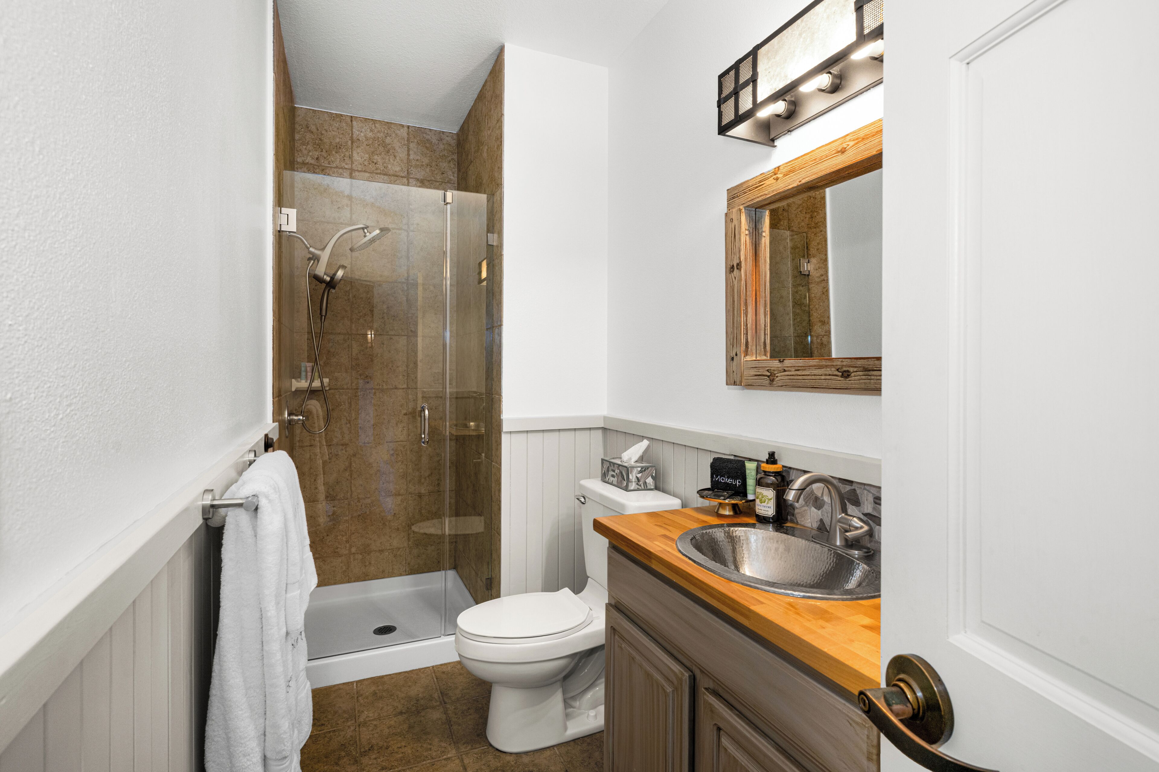 A bathroom with a shower, toilet, sink, and a mirror.