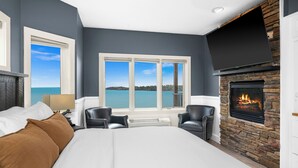 Ein Schlafzimmer mit Bett, Kamin, Meerblick und einem großen Fenster.