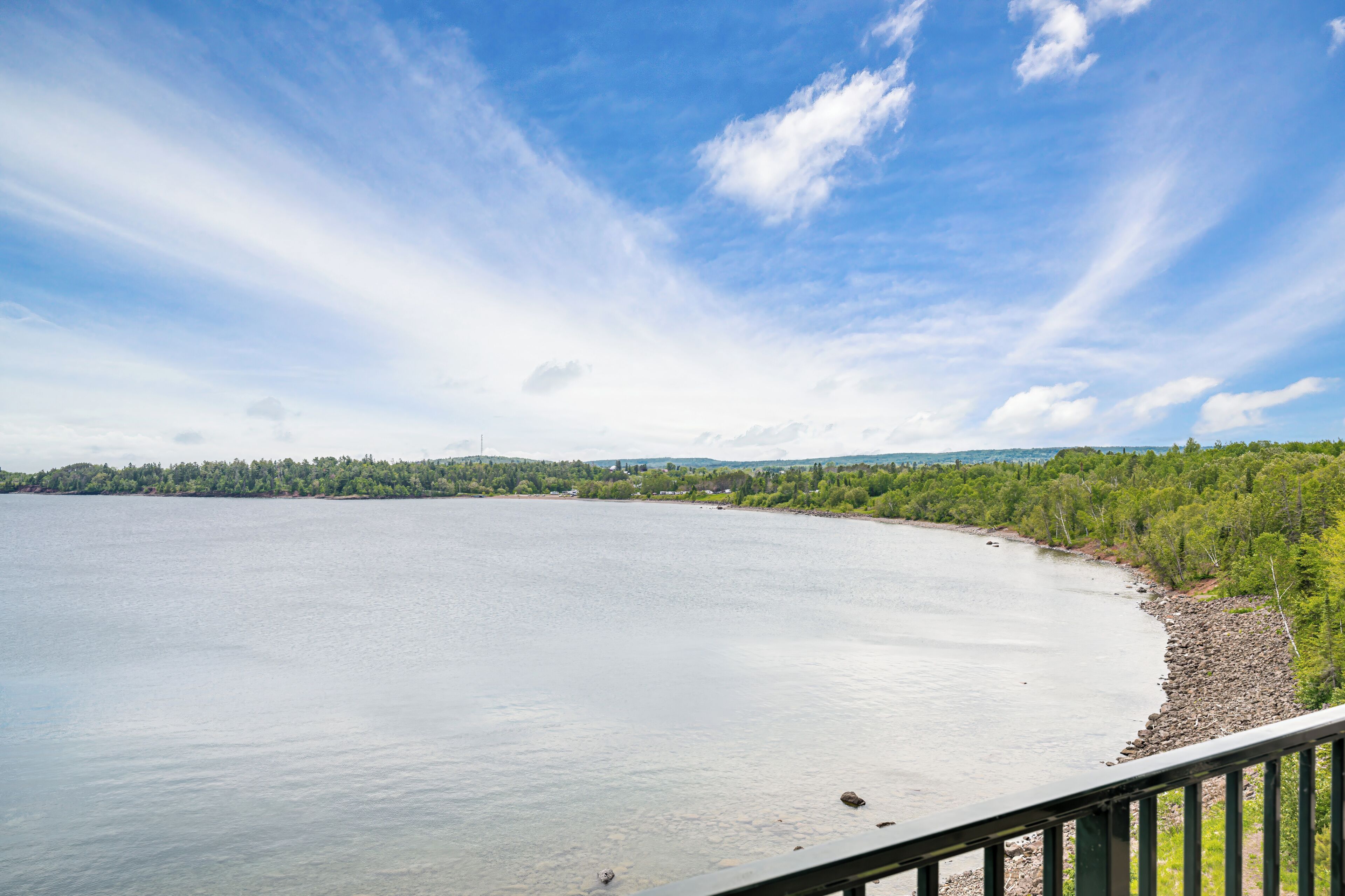 A calm lake with a forested shoreline, a clear sky, and a distant hill.