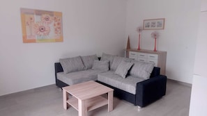 Una sala de estar con un sofá seccional gris, una mesa de centro de madera, un mueble con jarrones decorativos y un cuadro en la pared.