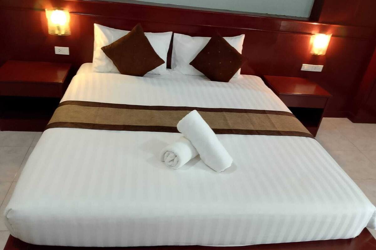 A neatly made bed with a striped bedspread, two pillows, and a rolled towel on the bed.