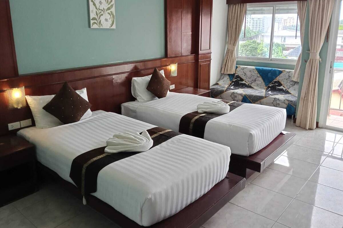 A hotel room with two beds, a sofa, and a window with curtains.