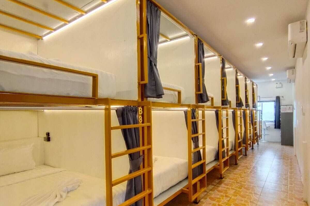 A row of bunk beds with wooden frames and white bedding, arranged in a corridor with tiled flooring.