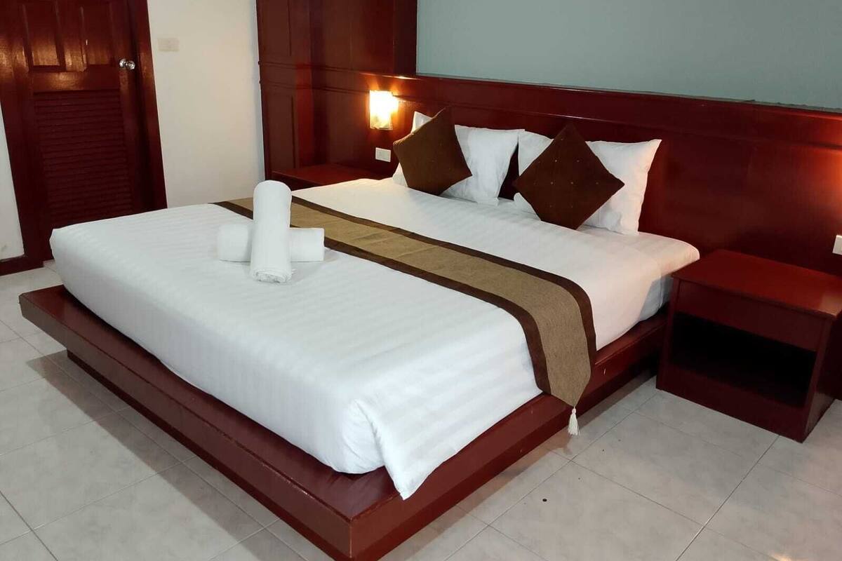 A hotel room with a large bed, a wooden headboard, a nightstand, and a wall-mounted light.