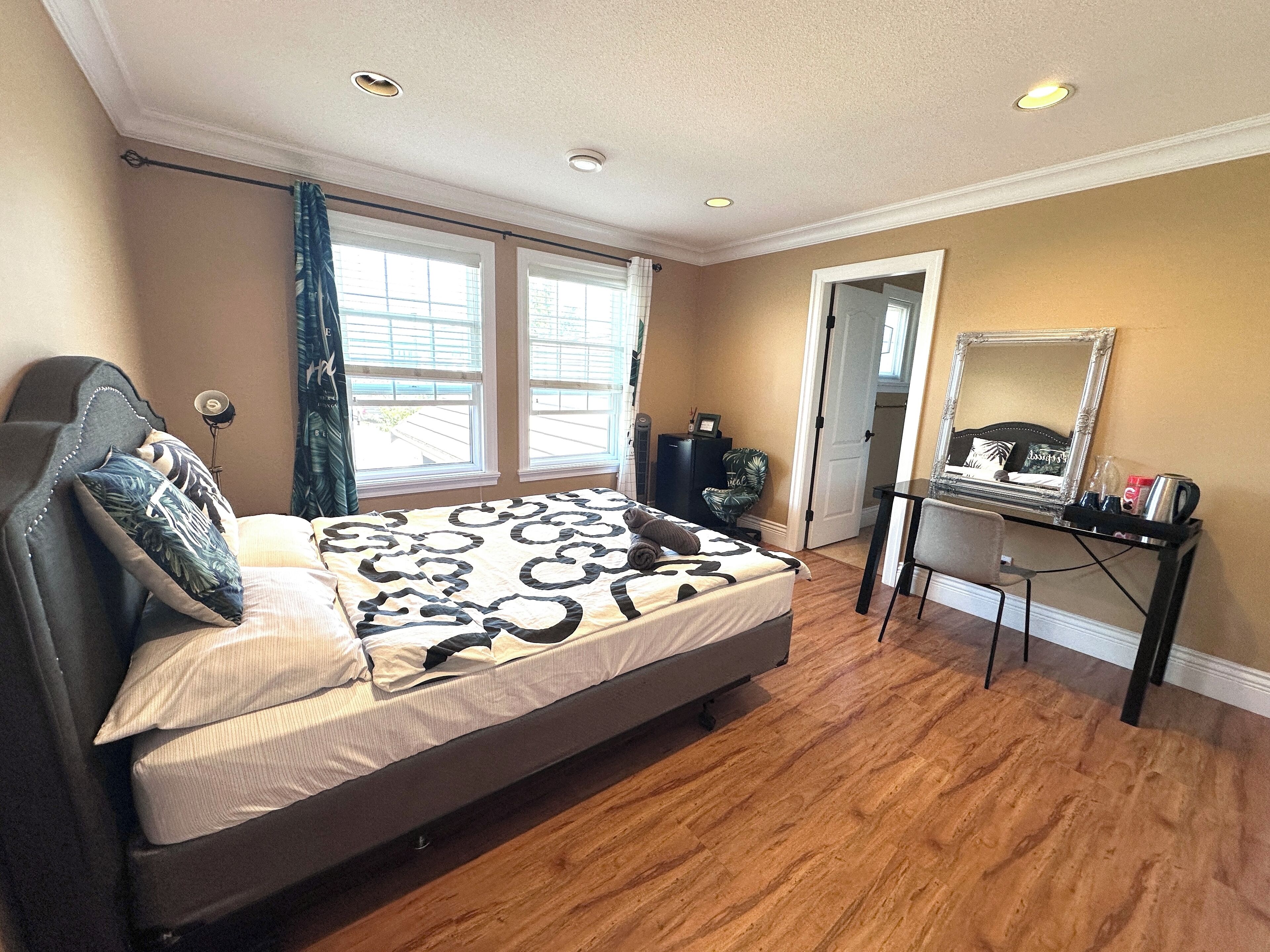 A bedroom with a bed, a desk, a chair, and a mirror.