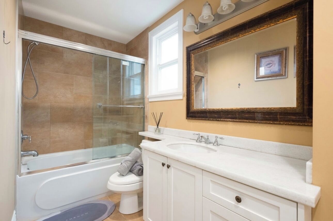 A bathroom with a glass-enclosed shower, a white bathtub, a toilet, and a large mirror above the sink.