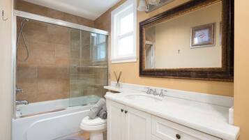 A bathroom with a glass-enclosed shower, a white bathtub, a toilet, and a large mirror above the sink.