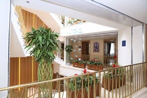 A modern hotel lobby with a staircase, potted plants, and a view of the interior.