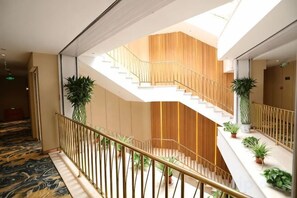 A hotel interior with a central staircase, potted plants, and a patterned carpet. - Super 8 Hotel (Beijing Qianmen Tiantan Park) (Beijing)