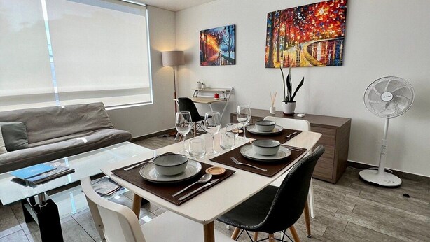 A modern dining area with a table set for four, a sofa, a standing lamp, and two paintings on the wall.