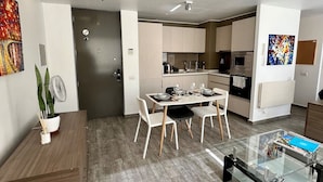 A modern kitchen with white cabinets, a dining area with a glass table, and a living room with a sofa and coffee table.