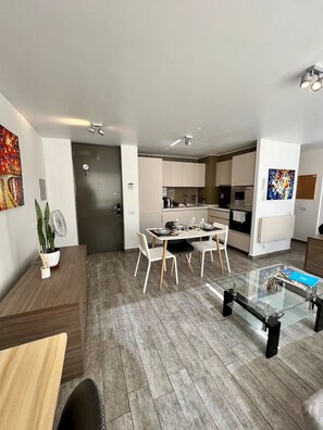 Eine moderne Küche mit weißen Schränken, ein Essbereich mit Glastisch und ein Wohnzimmer mit Sofa und Couchtisch.
