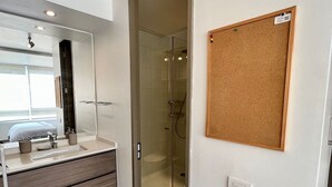 A modern bathroom with a glass shower, a mirror, and a corkboard on the wall.