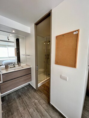 Ein modernes Badezimmer mit Glasdusche, Spiegel und Korktafel an der Wand.