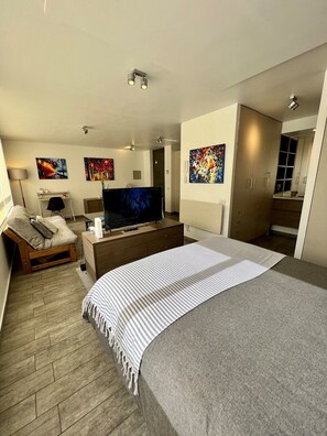 Ein modernes Schlafzimmer mit einem großen Bett, einem Fernseher, einem Schreibtisch und Bildern an den Wänden.
