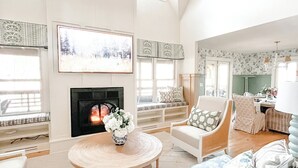 A spacious living room with a fireplace, a large sofa, and a dining area. - Lux 5BR w/ Theater, Fire-pit, Private Office + Guest Cottage, Close to Downtown (Highlands)