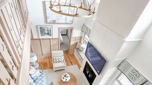 A spacious living area with a wooden floor, a sofa set, a coffee table, and a TV mounted on the wall.