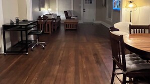 A spacious room with a wooden floor, a dining table with chairs, a sofa, a TV, and a lamp.