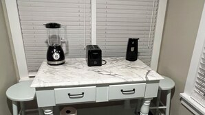 A kitchen counter with a blender, toaster, and speakers, with a marble countertop and a roll of paper towels.