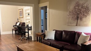 A spacious living room with a wooden coffee table, a leather sofa, and a piano in the background.