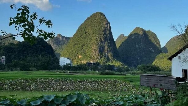 A rural landscape with a white building, lush greenery, and mountainous terrain.