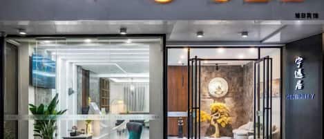 Entrada de hotel con fachada de vidrio, mostrador de recepción y un interior visible con asientos y decoración.