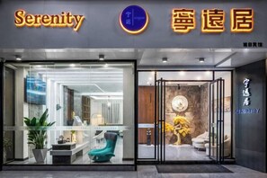 A hotel entrance with a glass facade, a reception desk, and a visible interior with seating and decor.