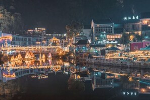 Een nachtzicht van een traditionele Chinese stad met verlichte gebouwen en een rivier die de lichten weerspiegelt.