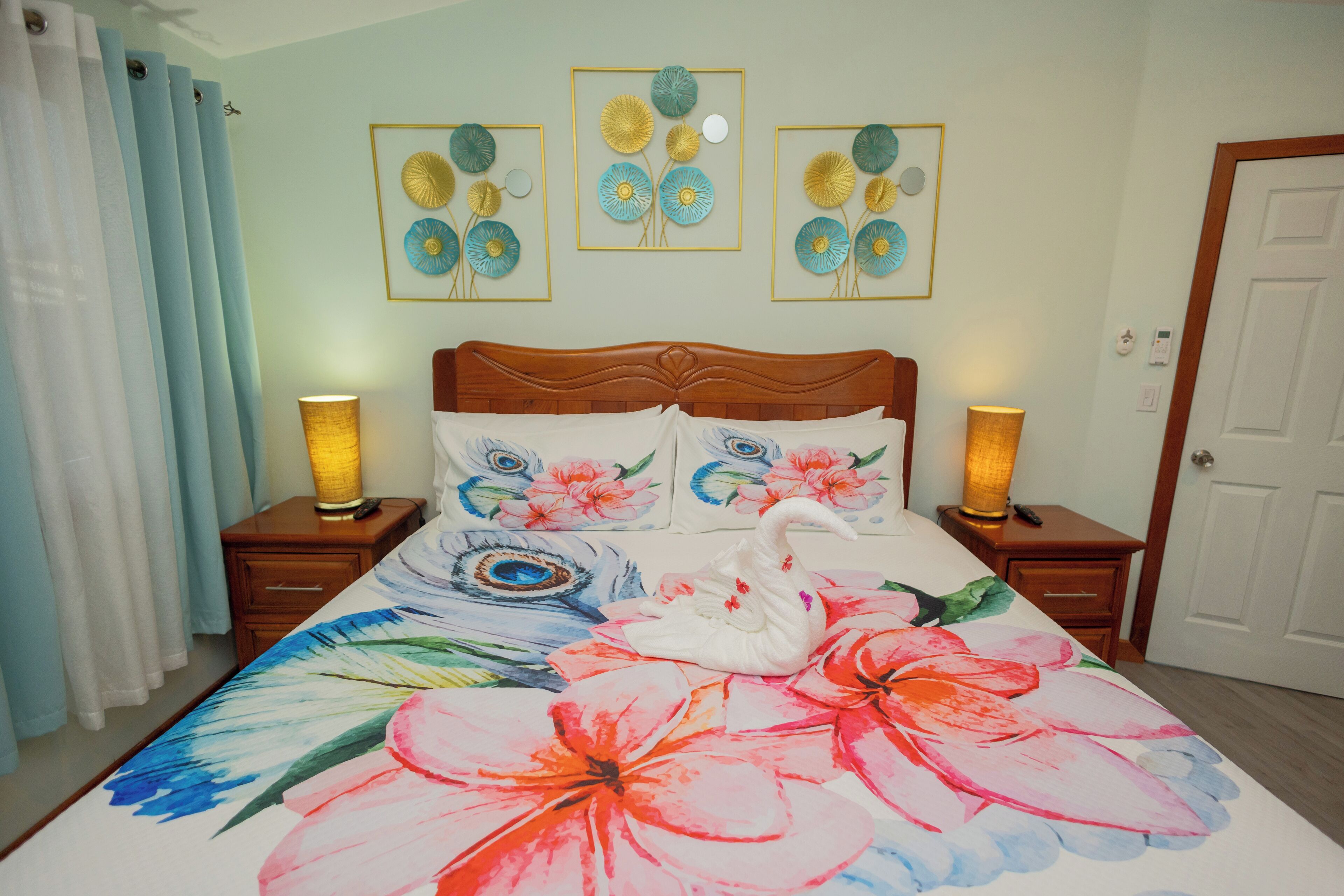 A bedroom with a floral bedspread, two bedside lamps, a wooden headboard, and three framed wall art pieces.