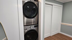 Une buanderie équipée de deux machines à laver à chargement frontal superposées, de meubles blancs et d’un plancher en bois.