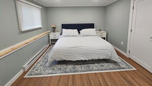 Une chambre à coucher comprenant un lit, des tables de chevet, une commode, une fenêtre avec des stores et une porte.