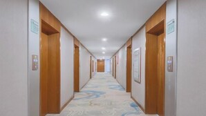Een hotelgang met houten deuren, een kamerbreed tapijt met dessin en inbouwverlichting.