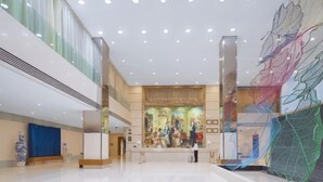 Een ruime lobby met een hoge plafond, een receptiebalie en een grote abstracte kunstinstallatie aan de rechterkant.