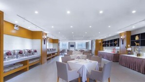 Een ruime restaurantzaal met meerdere tafels en stoelen, een vitrine met glazen en een goed verlicht interieur.