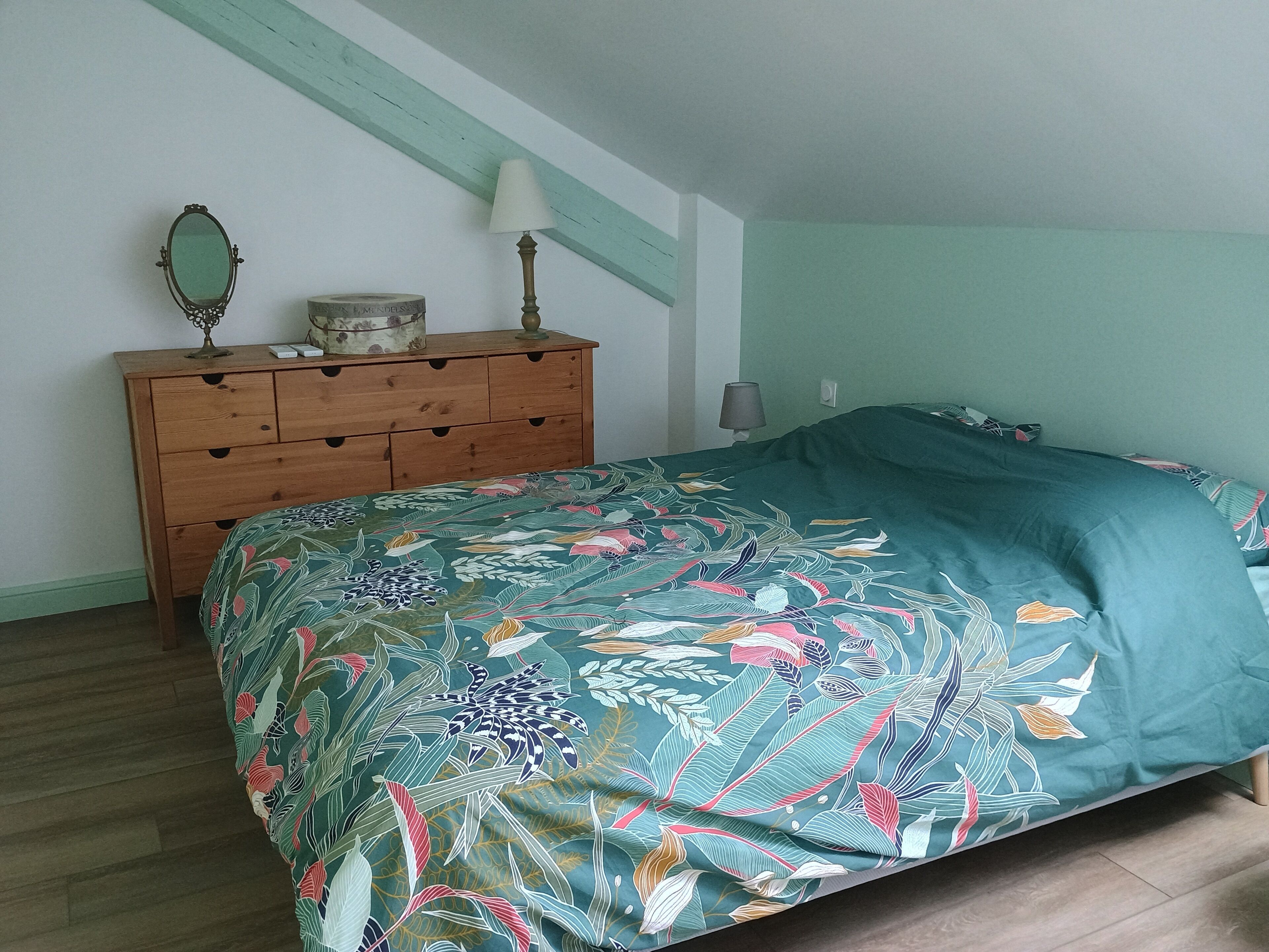 A bedroom with a bed, a wooden dresser, a mirror, and a lamp.