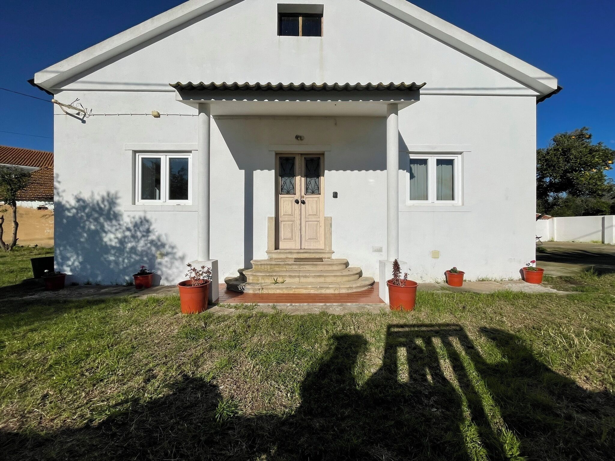 Una casa blanca de dos pisos amb un porxo, una porta de fusta i plantes en testos.